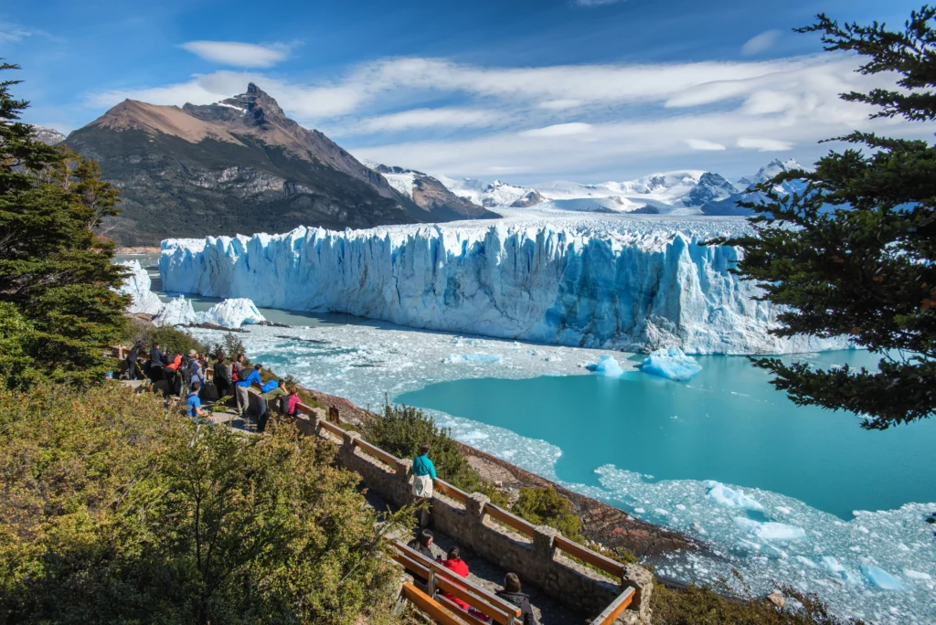 Foto de la gente mirando hacia un lago congelado alrededor de montañas llenas de nieve.