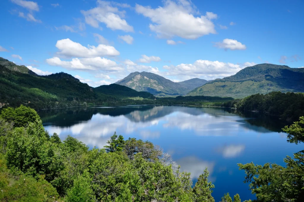 Foto del Lago Machónico, uno de los que vas a encontrar en el camino de los 7 lagos en auto, con el cielo azul reflejado en el agua y montañas al fondo.