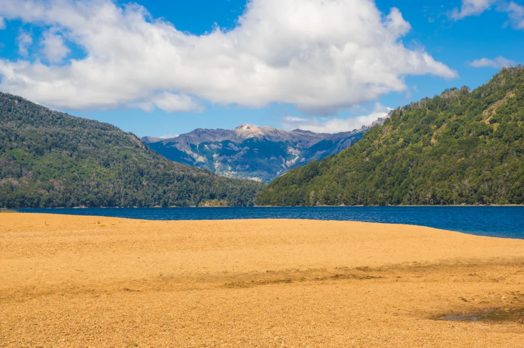 Foto del Lago Falkner, con arena en frente y montañas al fondo. Ese es un de los lugares que vas a conocer en el camino de los 7 lagos en auto.