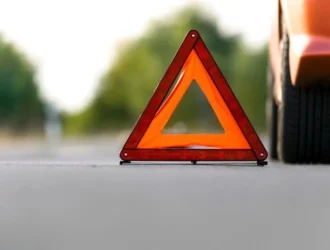 Image of a red car stopped on the road, with safety signage, waiting for car insurance