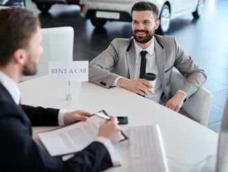 Two men in suits hold rental car documents at a car rental company.