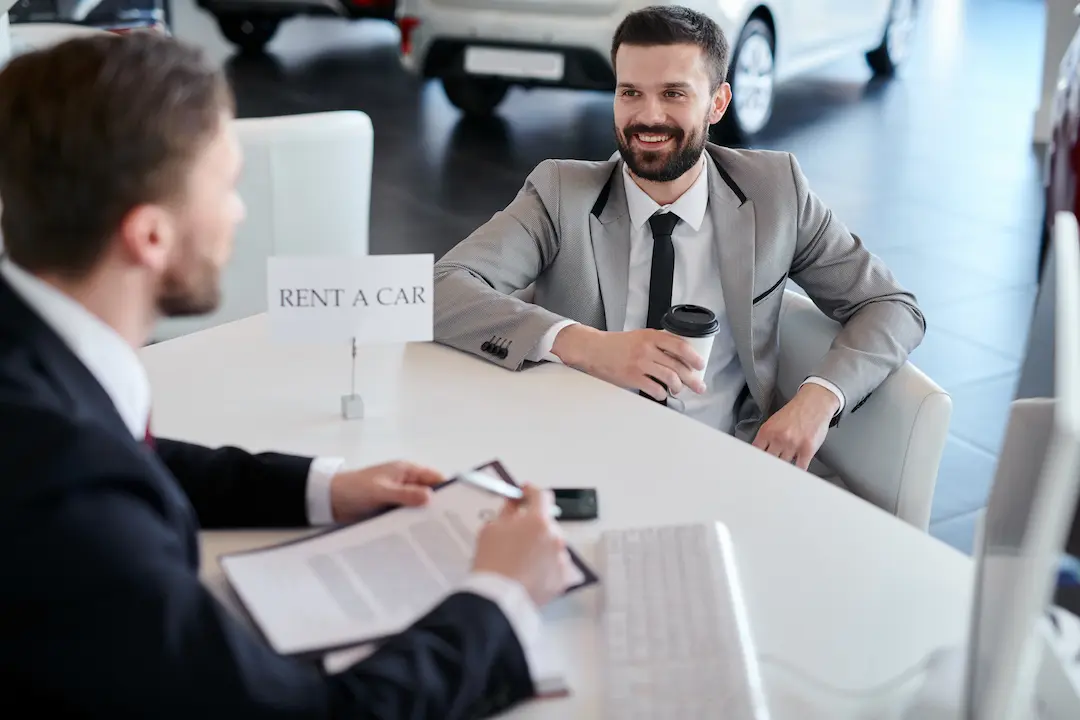 Two men in suits hold rental car documents at a car rental company.