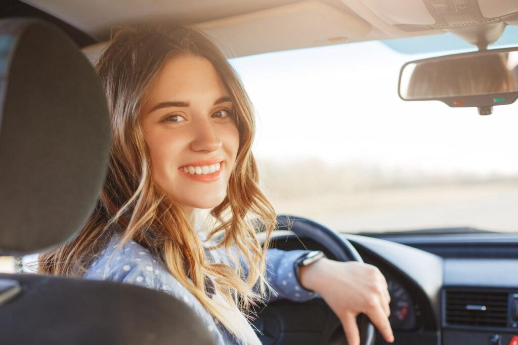 Jovem mulher sentada no banco de motorista do carro, sorrindo e olhando para trás. 