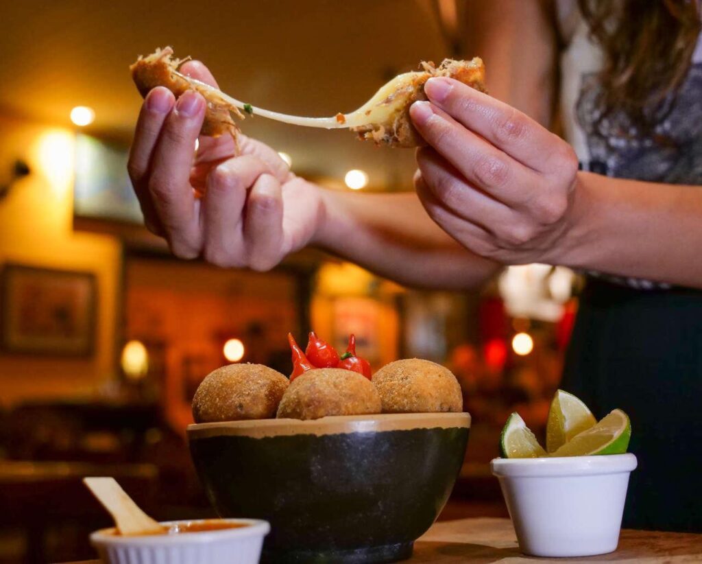 Mulher partindo um Bolinho de Costela, prato do restaurante Juanita, em Bonito. 