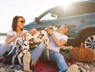 couple hugging a dog in front of a car