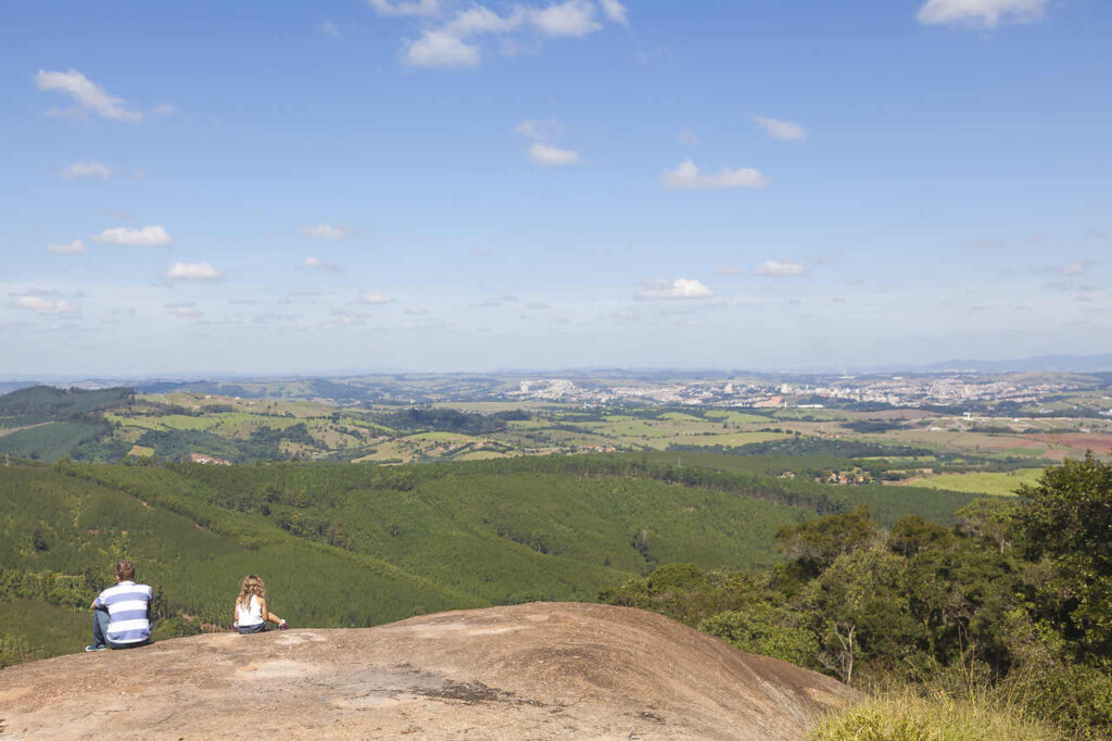 Um homem e uma menina sentados na parte mais alta do Pico das Cabras, apreciando a vista de Campinas.