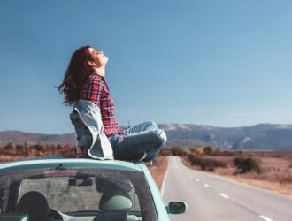 mulher sentada no teto do carro curtindo a paisagem da estrada