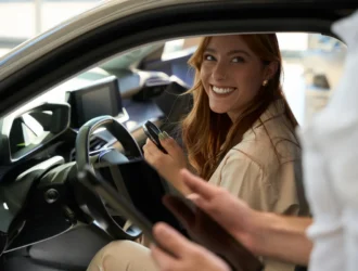 Mulher sorrindo dentro de um carro de aluguel mensal e do lado de fora o vendedor segura um tablet