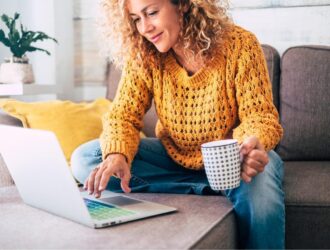 woman in yellow sweater with a mug in hand using a laptop