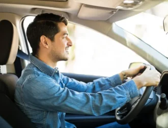 a man wearing a long sleve blue shirt driving a long term rental car