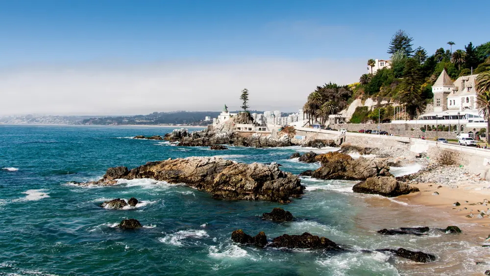 Foto de Viña del mar, con el mar en las rocas, algunas casas blancas y el cielo azul, un paisaje perfecto para una escapada romántica.