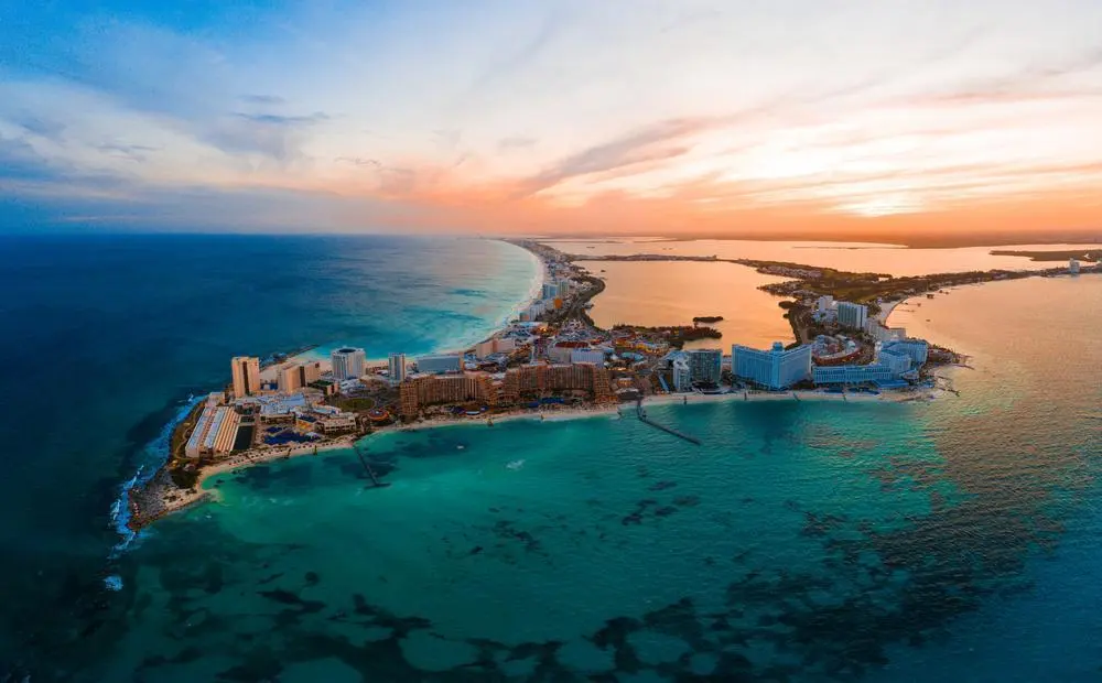 Foto de Cancún México com o mar ao redor. A cor é azul e é possível ver a cidade ao centro cheia de prédios.