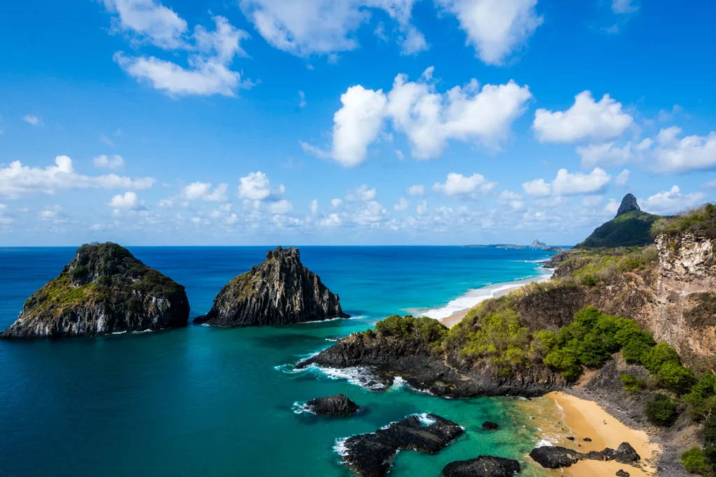 Baía dos Porcos, em Fernando de Noronha, vista de cima, o mar azul cristalino cercado por formações rochosas, cobertas por vegetação.