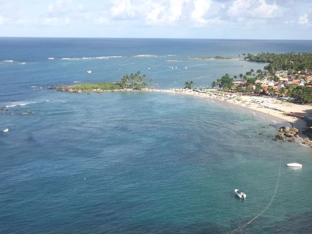 Foto aérea do Morro de São Paulo, na Bahia. O céu está azul com nuvens e o mar completamente azul.