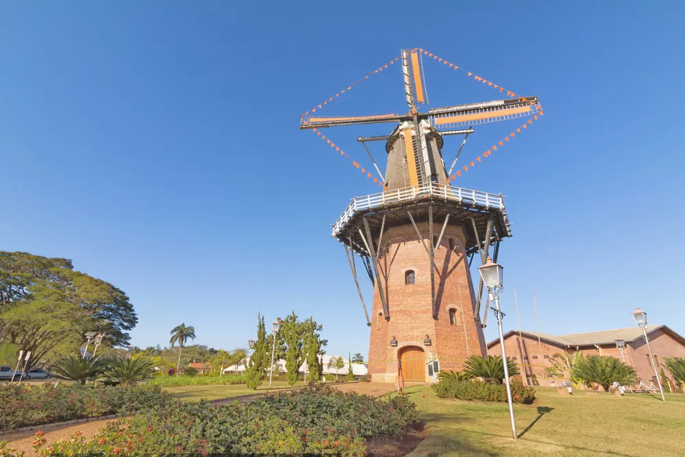Foto do Moinho de Holambra, em São Paulo. O céu está azul e é possível ver a vegetação verde em torno do moinho.