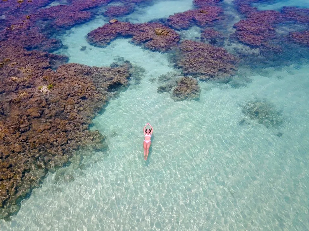 Foto de uma mulher nadando entre as piscinas naturais de Maceió. A água é cristalina e a piscina é bem rasa.