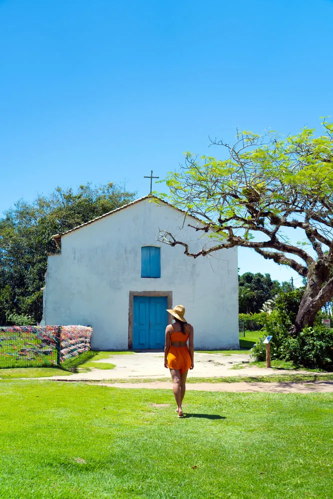 Foto de uma mulher de costas com uma paisagem atrás. Ao fundo conseguimos ver uma igreja de Porto Seguro na Bahia.