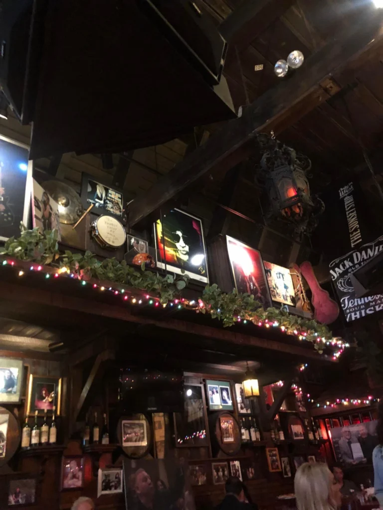 Foto do interior do bar Rainbow, um clássico do rock em Los Angeles. É possível ver fotos dos cantores do rock em quadros suspensos no alto. O interior é bem escuro e repleto de quadros.
