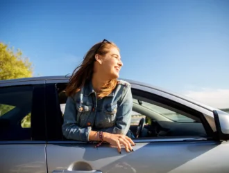mulher com a metade do corpo para fora do carro com luz do sol no rosto