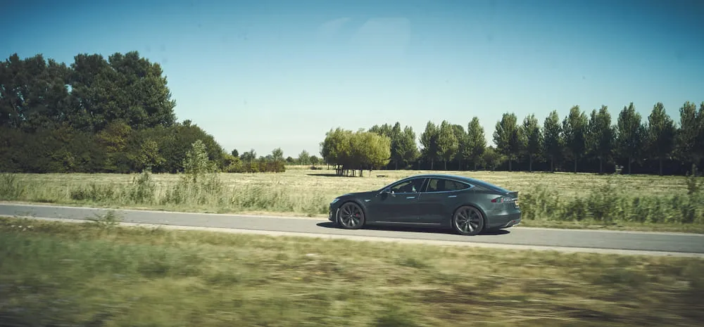 Carro em movimento pela estrada. O carro é sedan na cor preta.