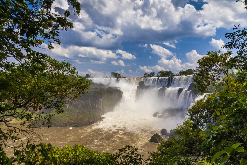 Foto das cataratas do lado argentino, no Parque Nacional Iguazú. O céu está azul e é possível ver a vegetação bem verde ao redor.