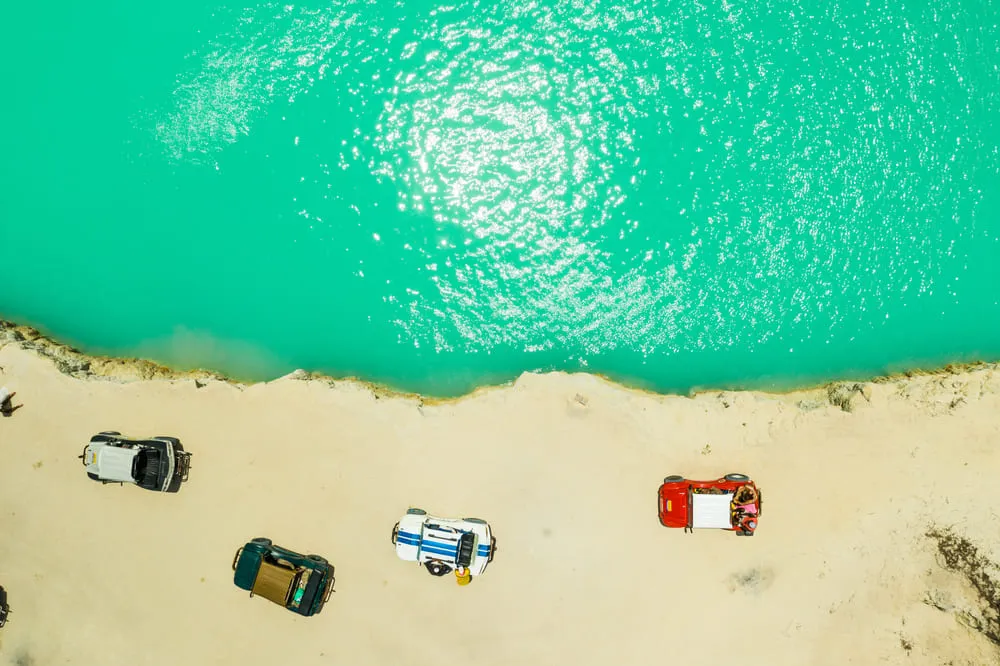 Foto de uma lagoa bem verde de Jericoacoara, região Nordeste do Brasil. Alguns buggys complementam a foto, estacionados na areia.