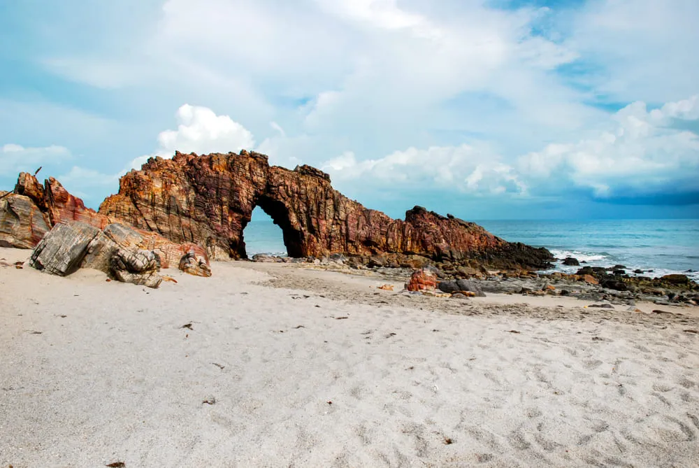 Foto da Pedra Furada em Jericoacoara, região Nordeste do Brasil. O mar e o céu estão na cor azul. 