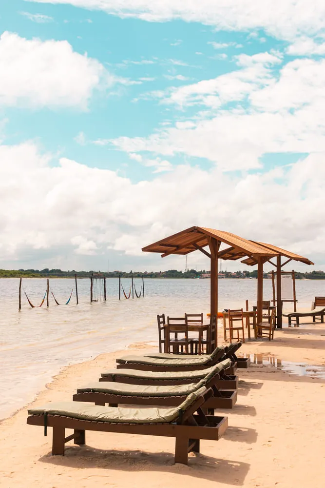 Foto de uma das praias de Jericoacoara, região Nordeste do Brasil. Há espreguiçadeiras lado a lado e algumas redes dentro do mar, na parte mais rasa. Há mesas e proteção solar para quem quiser comer ou beber algo de frente pro mar.