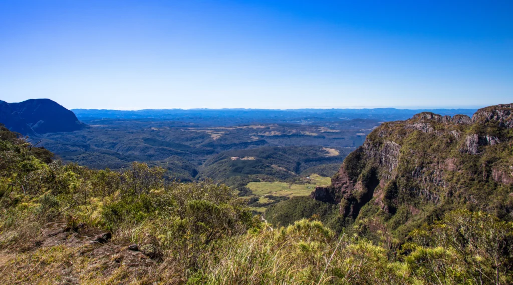 Foto aérea de Urubici na Serra Catarinense. É possível ver as montanhas impressionantes, o céu azul e a vegetação bem verde.