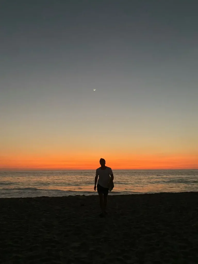 Foto con la silueta de un hombre contrastando con el atardecer en la playa Zicatela, lugar donde la gente practica surf, una de las 13 cosas que hacer en Puerto Escondido.