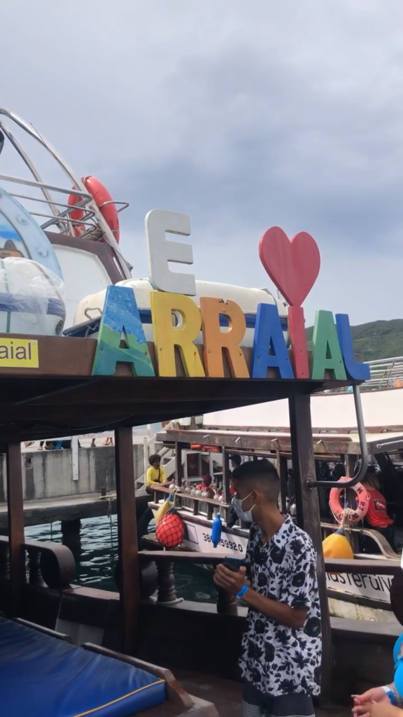 Foto em um passeio de barco em Arraial do Cabo. É possível ver a placa: Eu Amo Arraial e uma pessoa logo abaixo da placa. O céu está bem nublado.