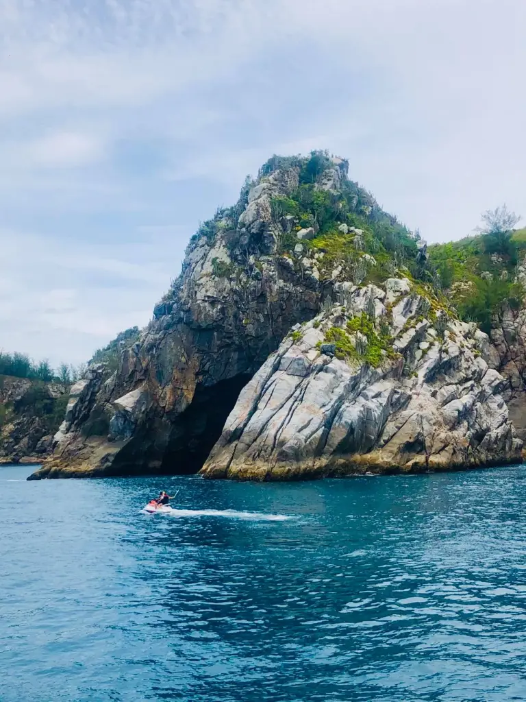 Foto da Gruta Azul em Arraial do Cabo. A foto foi tirada a partir da vista do passeio de barco realizado na região. O mar é bem azul e a rocha é imponente em meio ao mar.