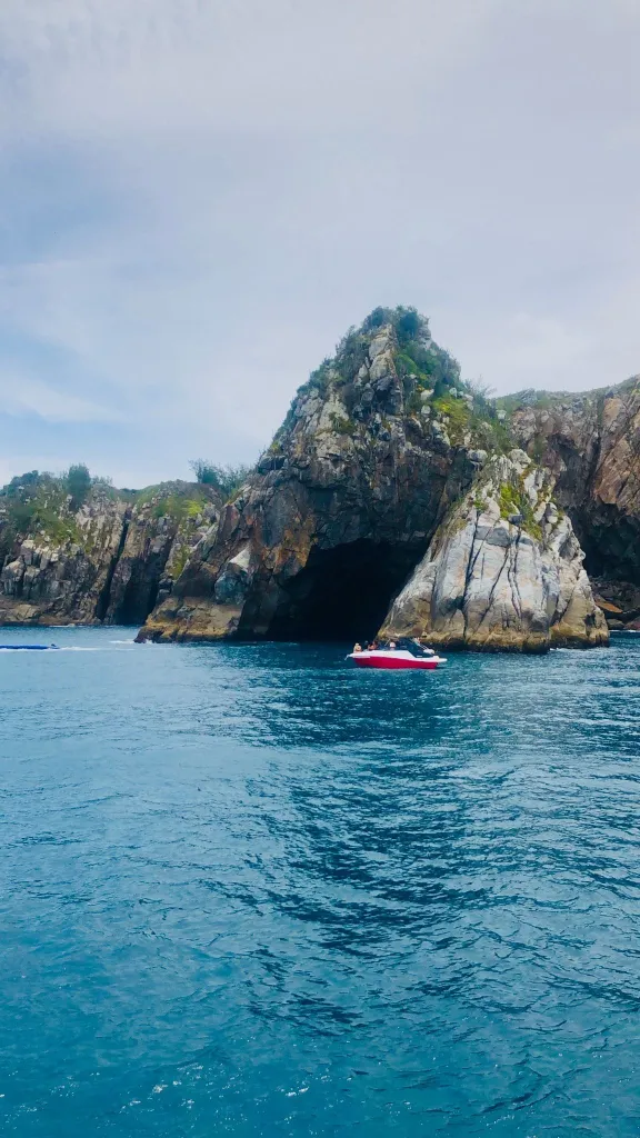 Foto da Gruta Azul em Arraial do Cabo. A foto foi tirada a partir da vista do passeio de barco realizado na região. O mar é bem azul e a rocha é imponente em meio ao mar.
