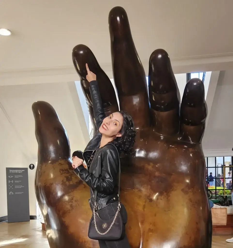 Foto de una mujer con el brazo levantado tocando con el dedo la punta de una escultura de mano gigante en un museo de Bogotá.