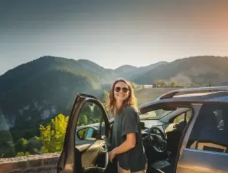 Foto de mujer en un mirador al lado de un carro abierto y con montañas en el paisaje.