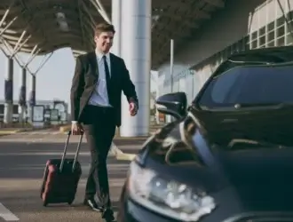 Foto de hombre en traje saliendo del aeropuerto con su maleta en dirección a su auto rentado para hacer turismo de negocios.