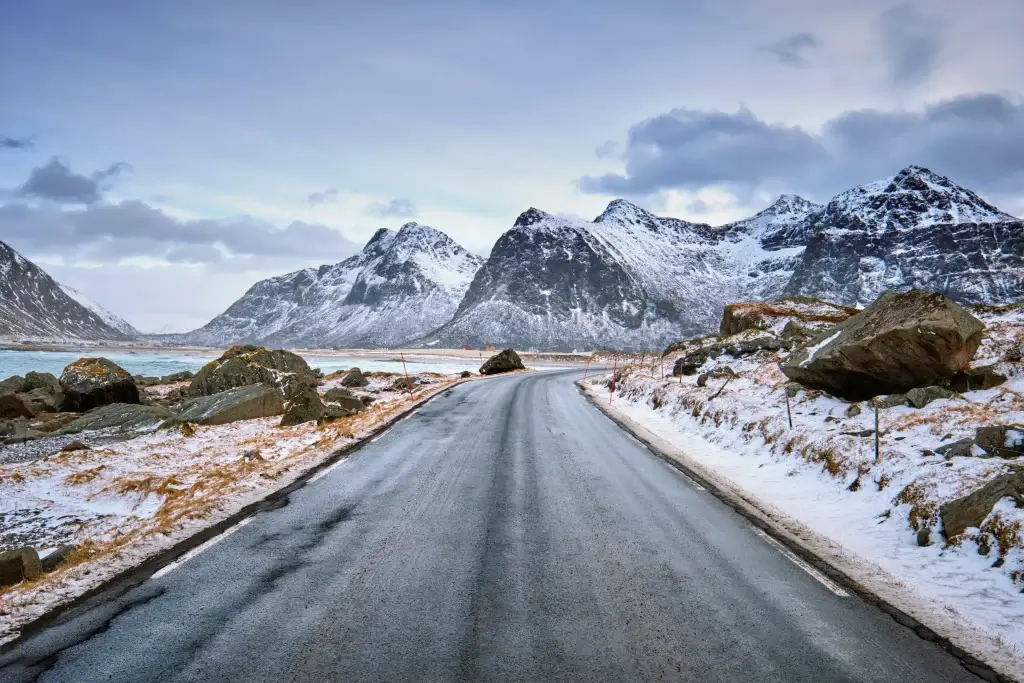 Foto de uma estrada nevada da Noruega. Nas laterais e ao fundo é possível ver pedras e montes nevados, com o céu bem claro.