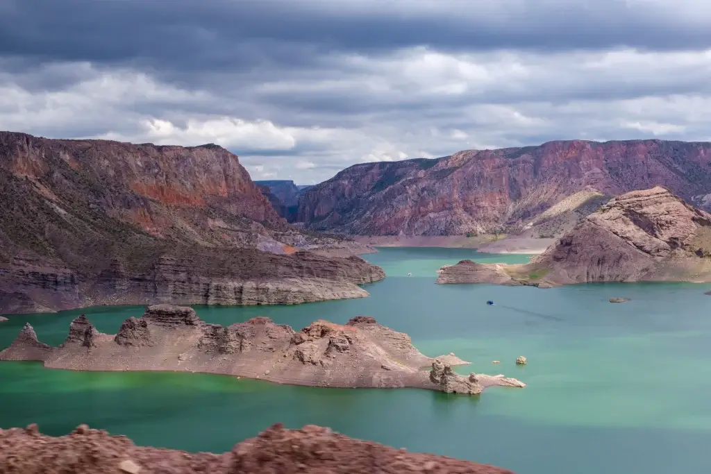 Foto aérea da região de Mendoza, Argentina. As montanhas ficam ao fundo e o céu está bastante nublado. A cor da água é verde e azul.