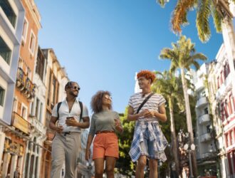 Foto de três amigos passeando pelas ruas de uma cidade. O céu está super azul e os prédios são coloridos.