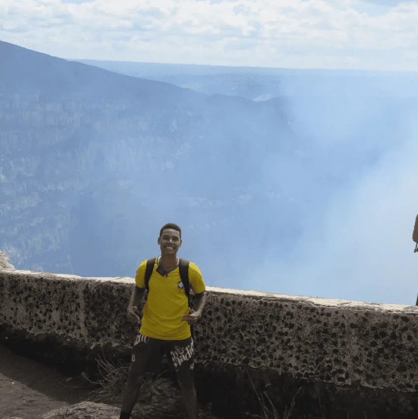 Foto por Helisson da Costa Menezes em sua viagem pela Guatemala. Ele está de camiseta do Brasil e sorri para foto, O fundo da foto está bastante nebuloso.