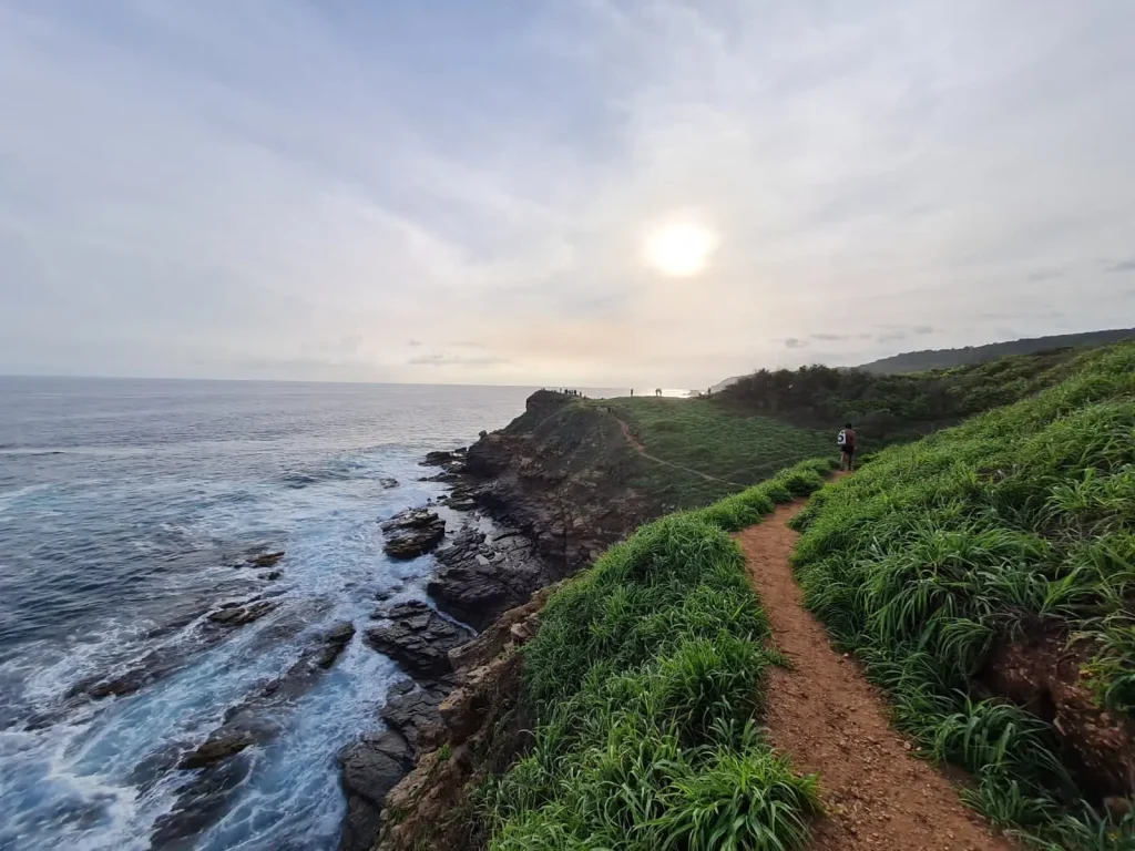 Foto da trilha de caminhada de Punta Cometa, uma das melhores coisas para se fazer em Puerto Escondido, com o sol escondido entre as nuvens e o mar à direita.