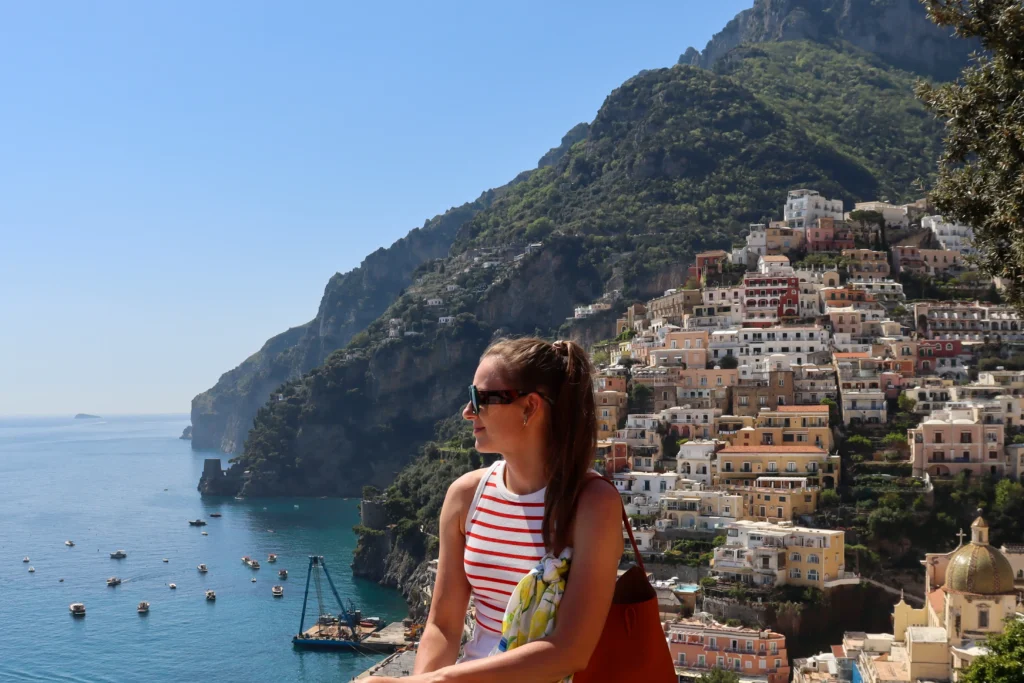 Young woman  stands on a viewing platform, looking out at the coastline of Positano.