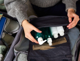 Uma garota coloca cosméticos em uma mala com roupas e acessórios para a viagem.